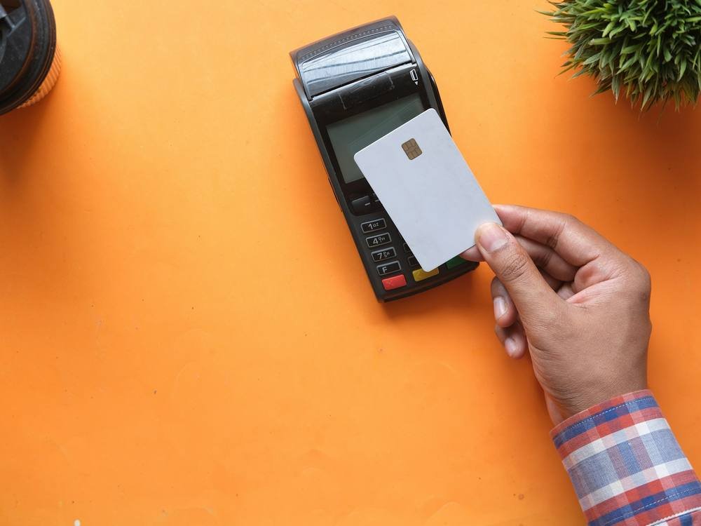 Mão aproximando um cartão de crédito da maquininha
